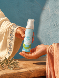AMAAN Duo gift moment · hand passing single AMAAN bottle, cream cotton sleeve with Berber indigo trim