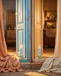 AMAAN Duo two homes · sky-blue door + cream door, AMAAN bottle on each threshold, one for you one for someone you love