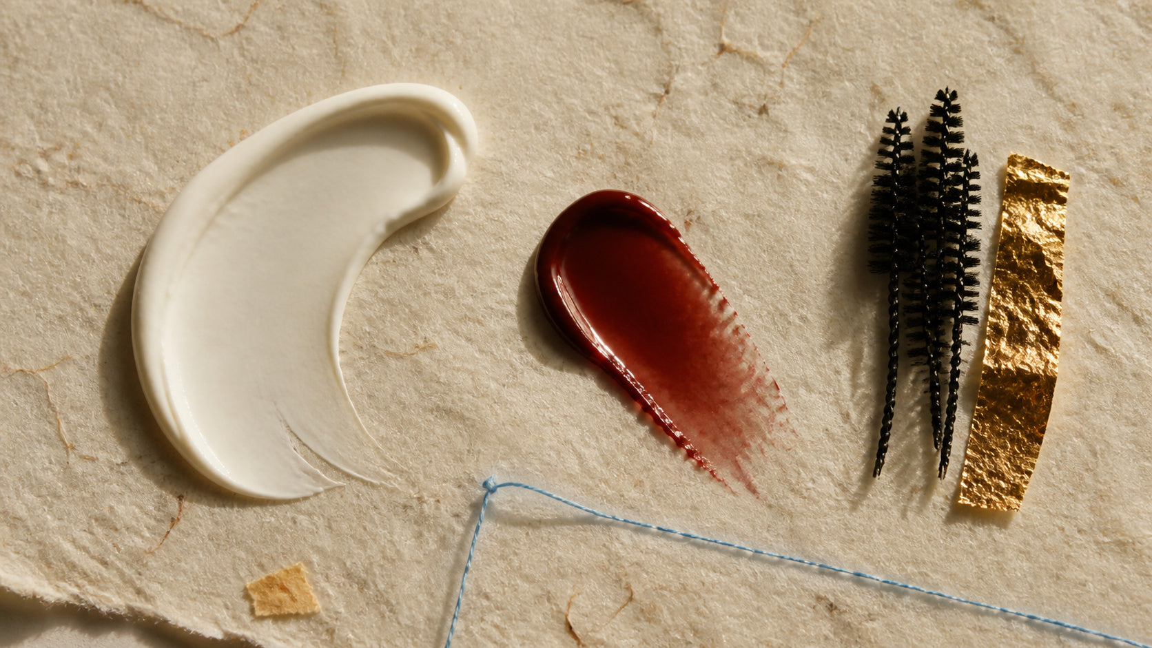 Material study of white cream, red balm, black fibres and a gold surface